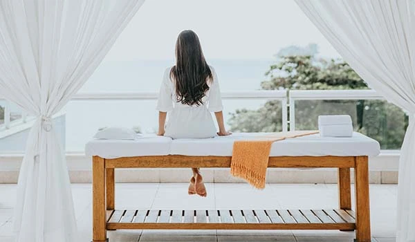 Mulher relaxando em uma área de spa com vista para o mar, representando tranquilidade e bem-estar no ambiente de um spa.