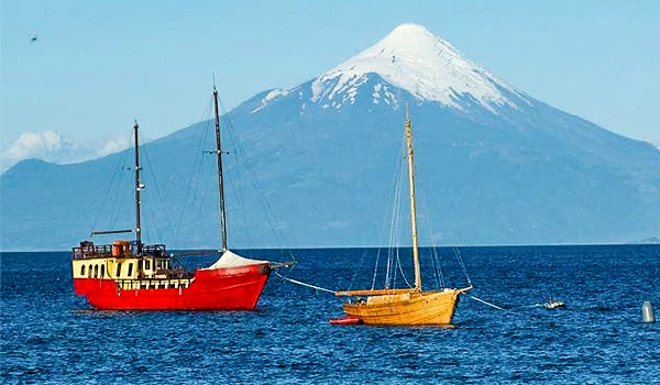 Cena de dois barcos em um lago uma imponente montanha com pico nevado, criando uma paisagem serena e pitoresca na Travessia dos Lagos Andinos.