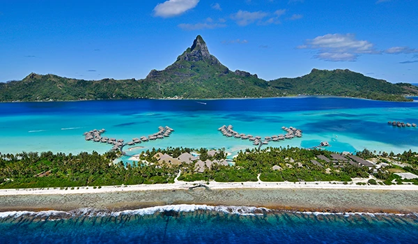 Vista aérea da ilha de Bora Bora na Polinésia Francesa, com águas cristalinas, bangalôs sobre a água e uma montanha icônica ao fundo. Um dos lugares para cerimônias de casamento e renovação de votos no exterior.