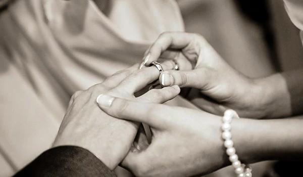 Imagem de uma troca de alianças de casamento, simbolizando união e amor entre duas pessoas. Cena de Casamento e renovação de votos no exterior.