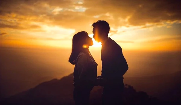 Casal apaixonado observando o pôr do sol no horizonte, com céu dourado e cenário ao ar livre, criando uma atmosfera romântica e encantadora. Casamento e renovação de votos no exterior.