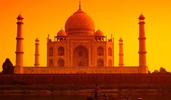 Imagem do Taj Mahal ao pôr do sol, com tons de laranja e amarelo, refletindo sua imponência e beleza na paisagem da Índia.