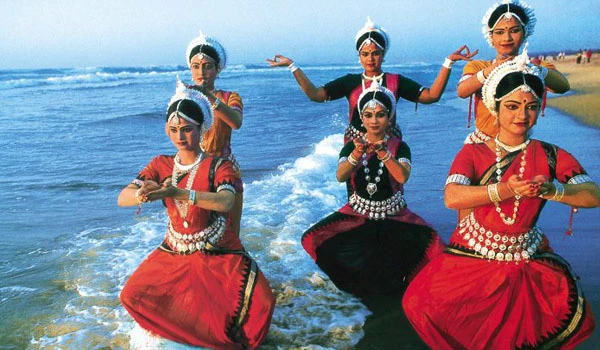 Grupo de dançarinas tradicionais hindus em trajes coloridos durante uma apresentação na praia, vedada de fundo azul do oceano