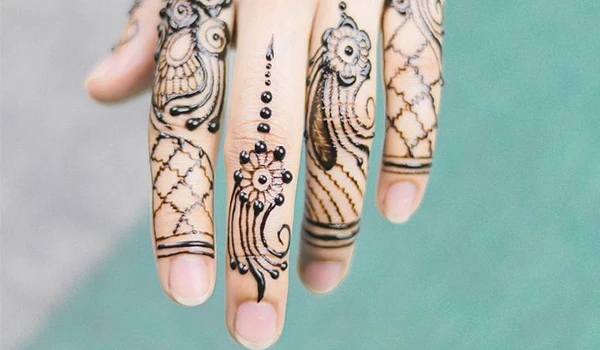 Mãos com tatuagens delicadas e detalhes em preto, evidenciando o design de henna ou tatuagem temporária, com fundo neutro que destaca a arte na pele.
