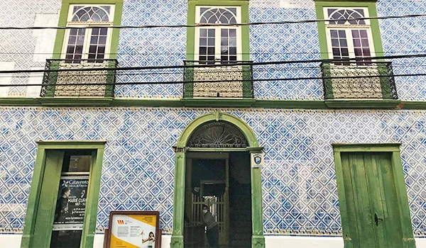 Foto de uma fachada de edifício histórico com azulejos azuis e brancos, com janelas e portas da cor verde.