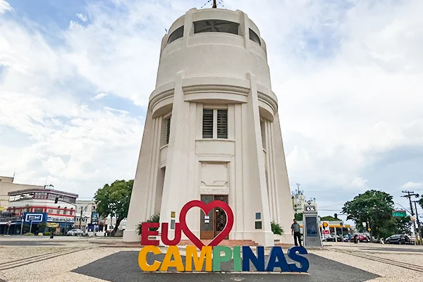 Foto da Torre do Castelo com letreiro a frente com os dizeres "Eu amo Campinas", cercado de pequenos prédios e carros. Local ideal para foto da Lua de Mel.
