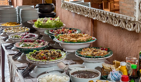 Mesa de saladas e pratos variados em restaurante, destacando a diversidade gastronômica com saladas frescas, acompanhamentos e molhos. Experiências em viajar para o Circuito das Frutas.