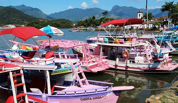 Embarcações coloridas de lazer no lago com montanhas ao fundo e céu claro, representando relaxamento na Lua de Mel em Paraty.