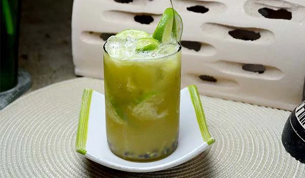 Copo de caipirinha decorado com limão e hortelã, colocado sobre uma mesa em ambiente descontraído.