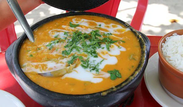 Imagem de uma tigela de sopa de abóbora quente decorada com creme, coentro e acompanhada de arroz branco ao lado, servida em uma mesa ao ar livre. Lua de Mel em Paraty.