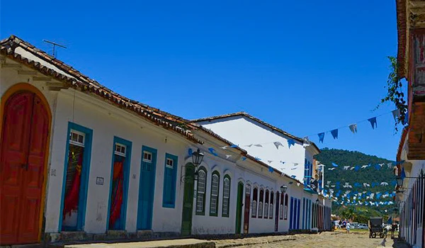 Imagem de uma rua colorida com casas tradicionais em Paraty, Rio de Janeiro, sob céu azul claro, decorada com bandeirinhas, mostrando o charme do centro histórico.