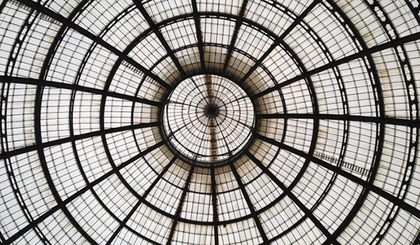 Vista de baixo para cima de uma grande cúpula de vidro e estrutura metálica, formada por painéis em formato radial.