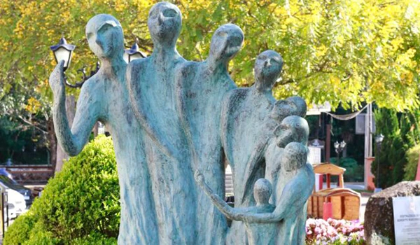 Imagem de uma obra de arte, feita de metais representando vários homens e uma criança, localizada em uma rua com área de lazer ao ar livre, ideal para turismo cultural e lazer. Lua de Mel em Santo Antônio do Pinhal.