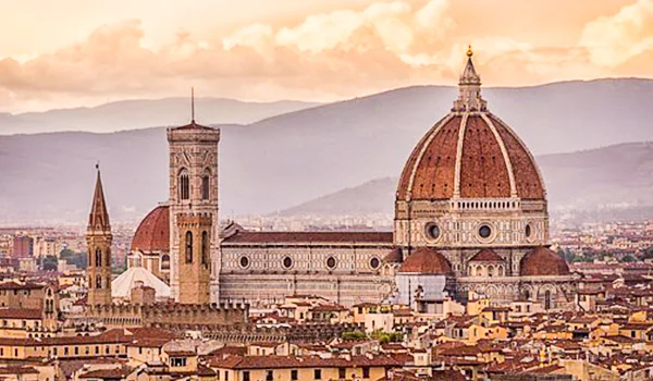 Vista panorâmica de Florença, na Itália, com a Catedral de Santa Maria del Fiore em destaque, incluindo sua grande cúpula de telhas vermelhas e a torre do campanário, cercada pelo casario da cidade e por colinas ao fundo. Lua de Mel na Itália.