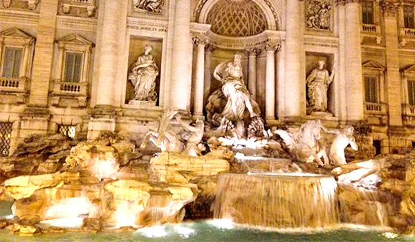 Fonte de Trevi, em Roma, iluminada à noite, com esculturas e água em primeiro plano. Lua de Mel na Itália.