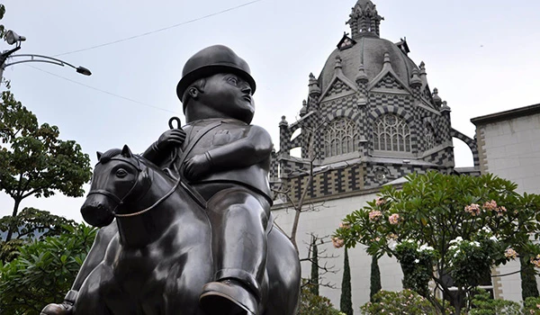 Estátua de um soldado em um cavalo localizada em frente a uma catedral histórica, cercada por árvores e flores, simbolizando história e cultura. Lua de Mel na Colômbia.