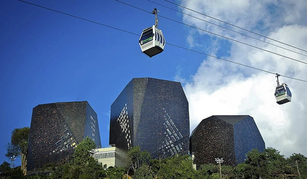 Imagem de uma cable car sobre com prédios modernos ao fundo e céu azul com nuvens. Lua de Mel na Colômbia.