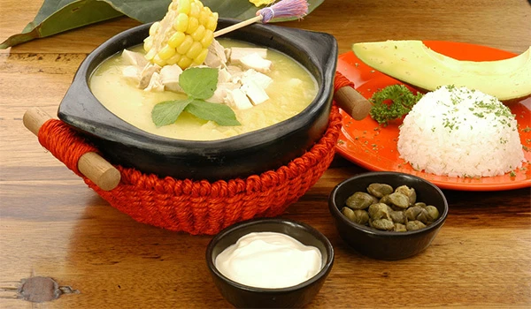 Prato de canjica com leite, acompanhado de arroz, abacate, azeitonas e creme de leite, típico da culinária brasileira, servido em uma mesa de madeira.
