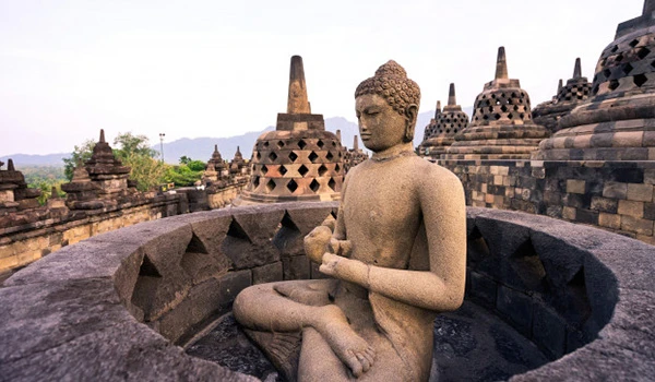 Imagem do Templo de Borobudur na Indonésia, mostrando uma grande escultura de Buda em posição de meditação rodeada por várias estruturas antigas do templo.