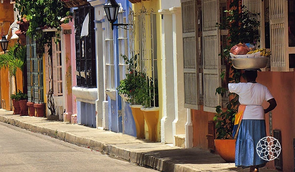Rua colorida com casas em tons pastel e uma pessoa carregando uma bacia na cabeça, refletindo a cultura vibrante do Brasil.