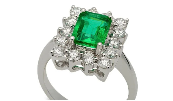 Anel de casamento com acabamento em prata ou ouro branco, centro com pedra esmeralda oval e cercado por diamantes brilhantes, elegância e luxo.
