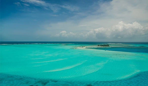 Vista panorâmica de uma paisagem tropical com águas cristalinas, recifes de corais e pequena ilha em uma manhã ensolarada.