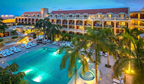 Imagem de um resort com piscina ao ar livre, áreas de lazer com espreguiçadeiras, muitas palmeiras e um edifício de vários andares ao pôr do sol, ideal para férias na praia. Lua de Mel na Colômbia.
