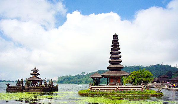 Imagem de um templo tradicional na Indonésia situado em uma ilha com água ao redor, cercado por natureza exuberante e céu nublado, representando cultura e história. Casamento em Bali.