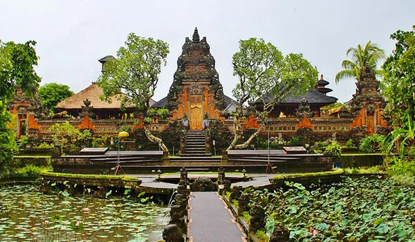Imagem de um templo antigo de arquitetura tradicional na Indonésia, rodeado por águas com lírios, árvores verdes e um jardim bem cuidado, refletindo tranquilidade e beleza cultural. Casamento em Bali.