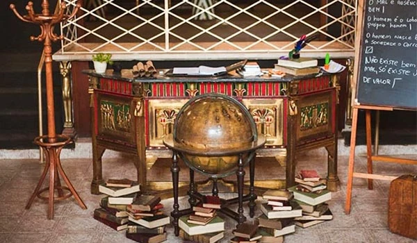 Imagem de um escritório com uma escrivaninha antiga, livros empilhados no chão e um globo em frente à mesa. Harry Potter em Campos do Jordão.