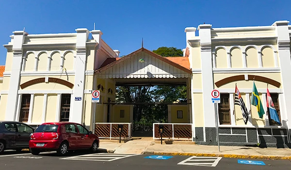 Fachada do histórico prédio em estilo neoclássico, com detalhes arquitetônicos e bandeiras expostas na entrada, em um dia ensolarado.