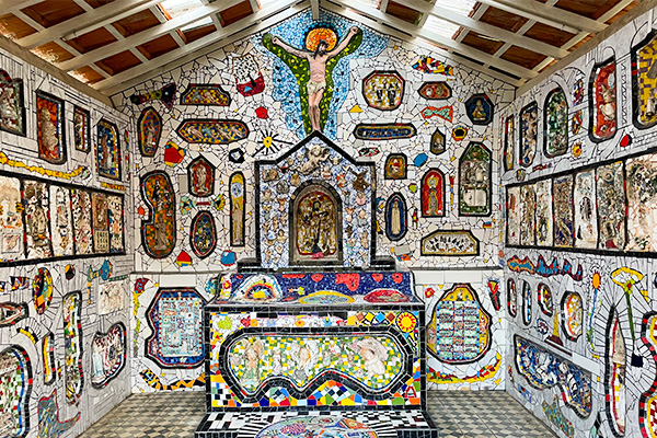 Interior de uma capela decorada com mosaicos coloridos e retratos religiosos, com destaque para a imagem de Jesus Cristo na parede do fundo.  O que fazer em São Bento do Sapucaí.