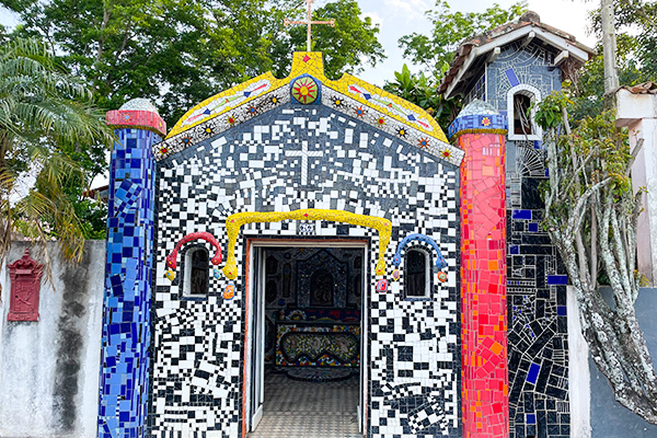 Fachada colorida capelinha com mosaicos de azulejos coloridos em diferentes tonalidades, com detalhes artísticos e elementos de decoração variados.  O que fazer em São Bento do Sapucaí.