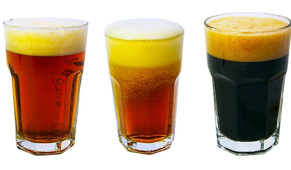 Três copos de cerveja artesanal em diferentes cores, com espuma cremosa no topo, representando variedade de estilos de cerveja.  O que fazer em São Bento do Sapucaí.