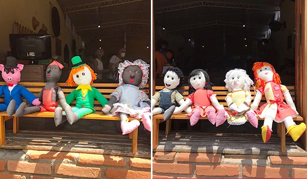 Bonecas artesanais de pano com roupas coloridas, sentadas em um banco de madeira em ambiente interno, consideradas brinquedos artesanais para crianças.
