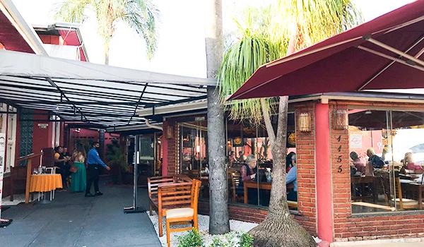 Imagem de um restaurante ao ar livre com mesas e cadeiras, palmeiras ao fundo, criando uma atmosfera agradável e acolhedora.