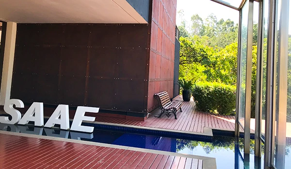 Imagem de uma área externa moderna com piscina e a placa do SAAE. O ambiente é bem iluminado, cercado por vegetação e mobiliário contemporâneo.