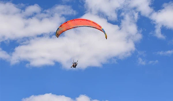 Parapente colorido voando sob céu claro com nuvens brancas, perfeito para atividades ao ar livre e aventuras de aventura em alta altitude.  O que fazer em São Bento do Sapucaí.