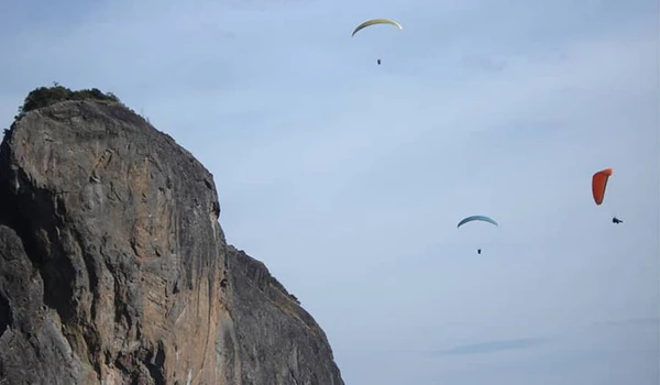 Parapentes sobrevoando uma formação rochosa em um dia claro, com céu parcialmente nublado.  O que fazer em São Bento do Sapucaí.