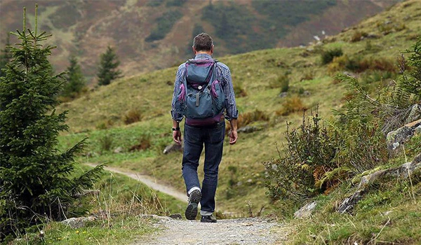Homem com mochila caminhando por trilha em meio a natureza, com árvores e vegetação, perfeito para aventuras ao ar livre e trekking na natureza.  O que fazer em São Bento do Sapucaí.