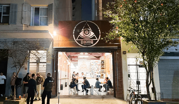 Foto da entrada do Bar Dogma, com clientes sentados no interior e vários outros na calçada.