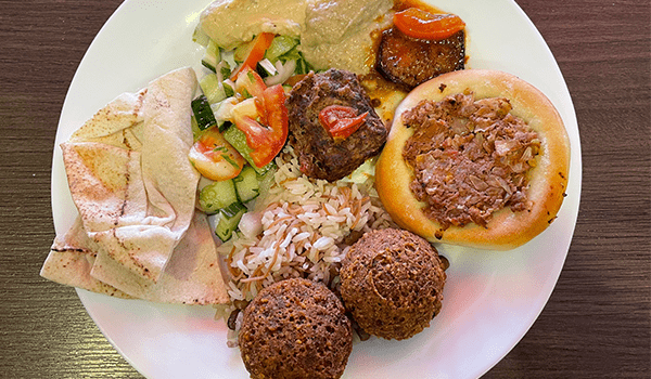 Foto de comida com faláfel, esfirra, salada, e outros itens da culinária palestina do restaurante Majáz.