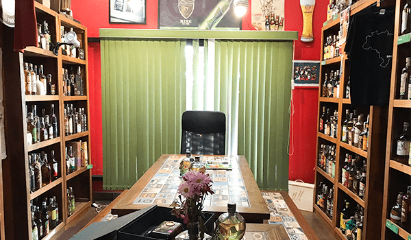 Foto de uma mesa no meio de estantes com cachaça, no primeiro andar, onde são feitas degustações do Bar Rota do Acarajé.
