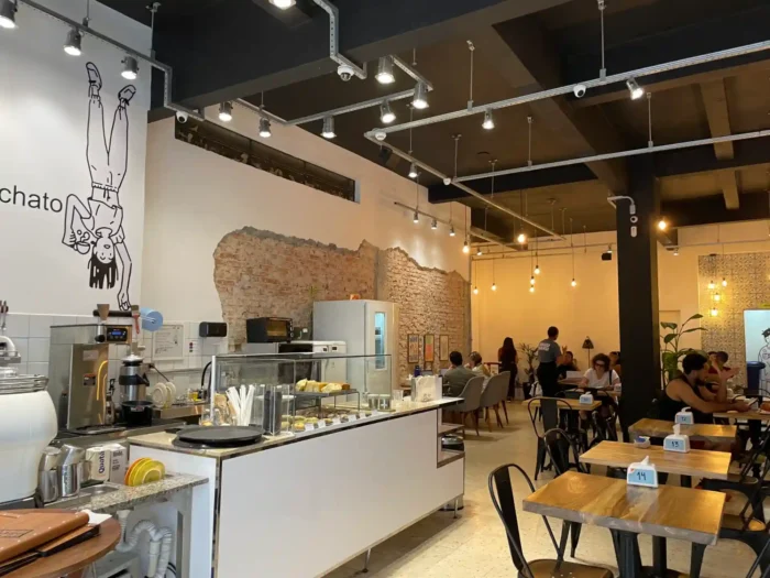 Foto da Waku Waku cafeteria, onde aparece mesas com clientes, balcão com produtos e paredes com tijolos aparentes.