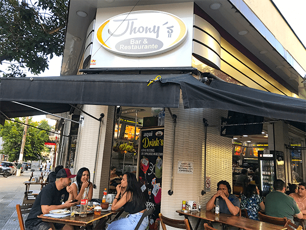  Foto da entrada do Jhony´s com mesas na calçada com clientes, um dos bares da Santa Cecília mais populares.