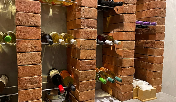 Prateleira com várias garrafas de vinho organizadas em paredes de tijolos expostos em adega elegante, ideal para armazenamento de bebidas.
