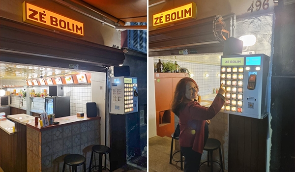Máquina de vendas automática na loja Zé Bolim, com pessoa comprando um produto, ambiente com iluminação quente, móvel de atendimento e painel de controle moderno.