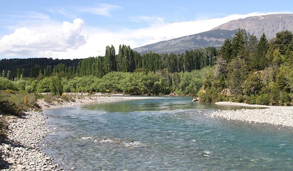 Foto de um rio cercado de vegetação e montanhas na província de Chubut na Argentina.