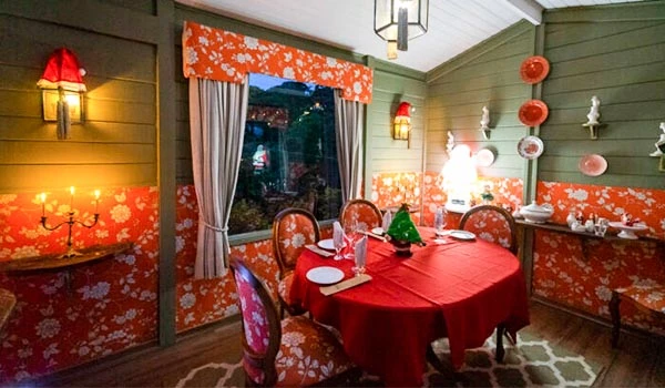 Salão de jantar decorado com tema floral laranja e rosa, com mesa redonda, cadeiras, cortinas elegantes, luminárias vintage e decoração charmosa. Natal em Campos do Jordão.