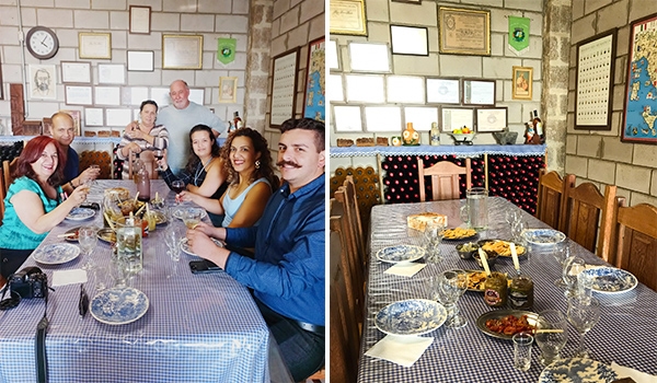 Imagem de um grupo de pessoas reunidas em uma mesa com pratos de comida em um ambiente acolhedor, decorado com quadros e prêmios. Vinícola Chão de Pedra.